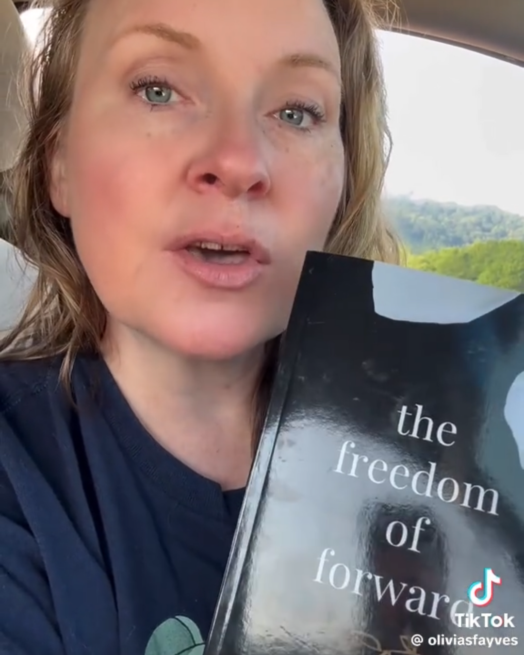 Person holding a book titled 'The Freedom of Forward' by Morgan Richard Olivier inside a vehicle.